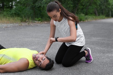 Young woman checking pulse of unconscious man in park