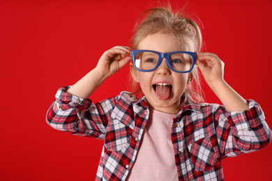 Photo of Funny little girl with glasses on red background. April fool's day