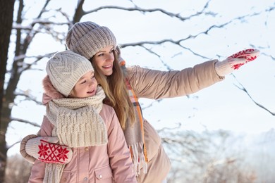 Family time. Mother showing something to her daughter in sunny snowy forest