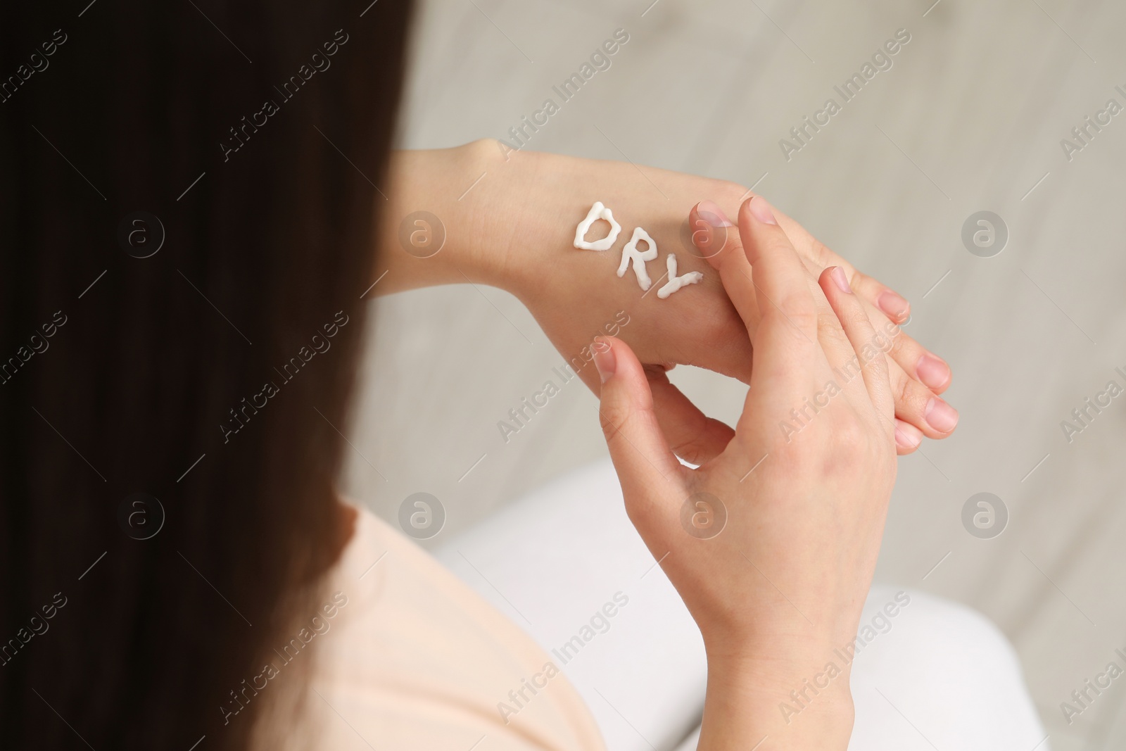 Photo of Young woman with word Dry made of cream on her hand indoors, closeup