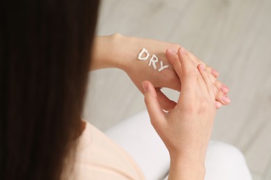 Young woman with word Dry made of cream on her hand indoors, closeup