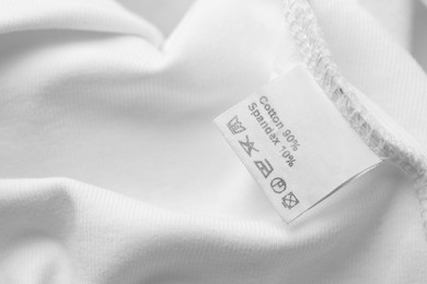 Photo of Clothing label with care recommendations on white garment, closeup. Space for text