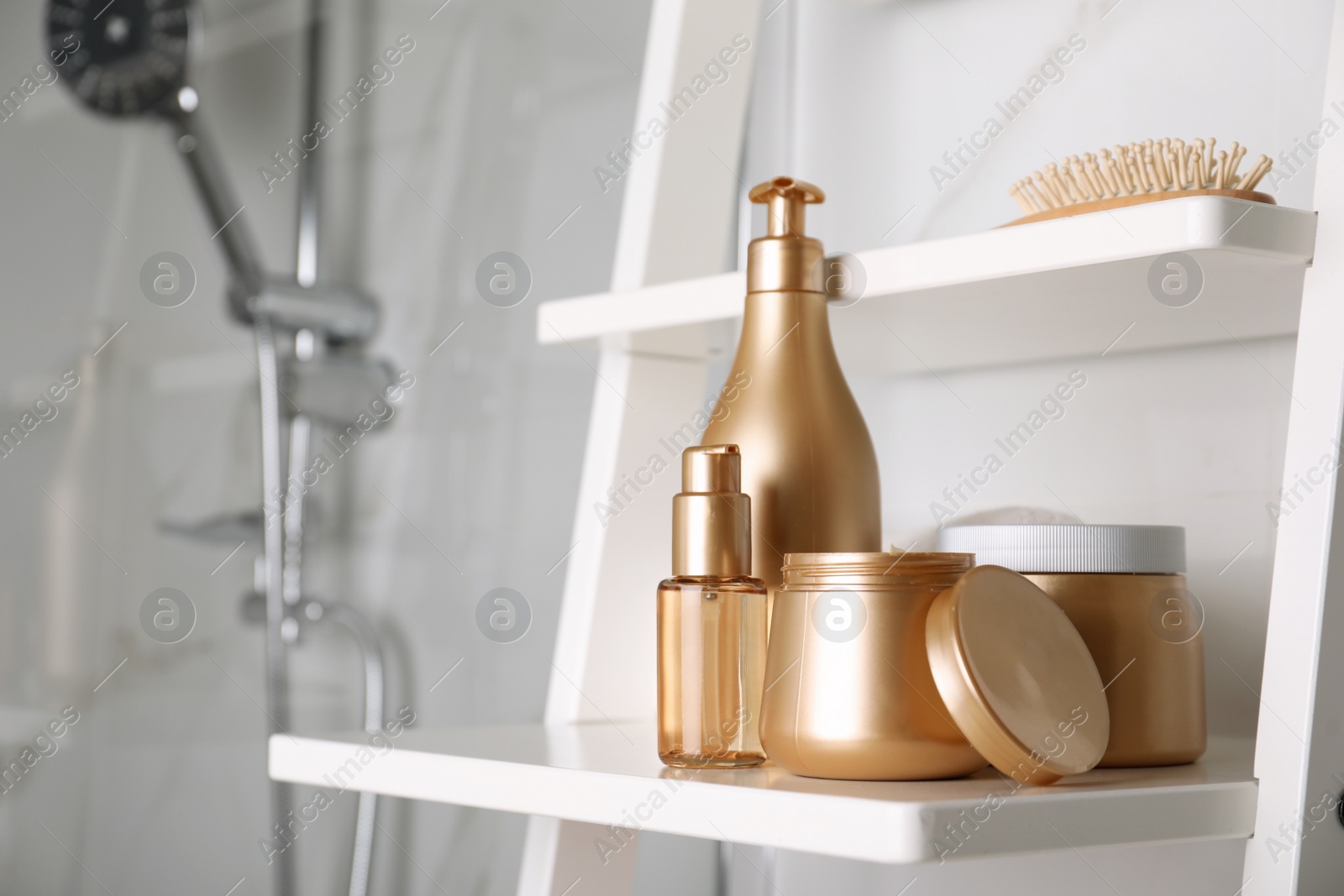 Photo of Different hair care products and brush on shelving unit in bathroom
