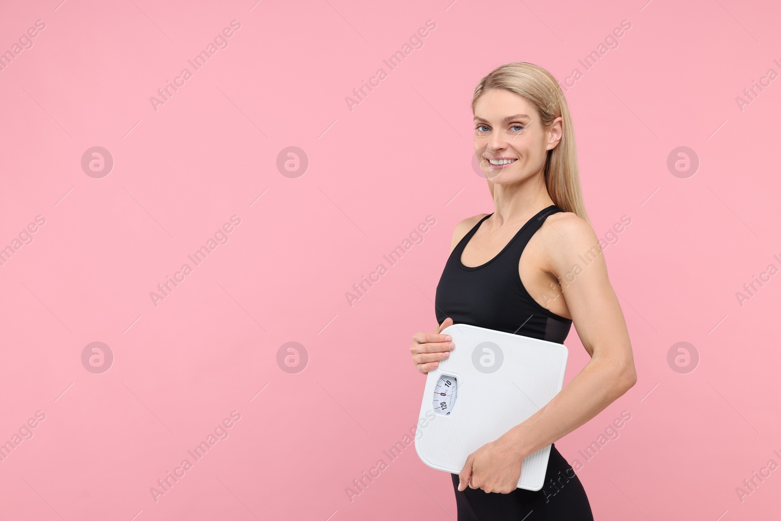 Photo of Slim woman holding scales on pink background, space for text. Weight loss