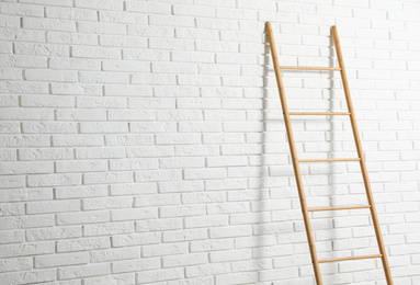 Modern wooden ladder near white brick wall. Space for text