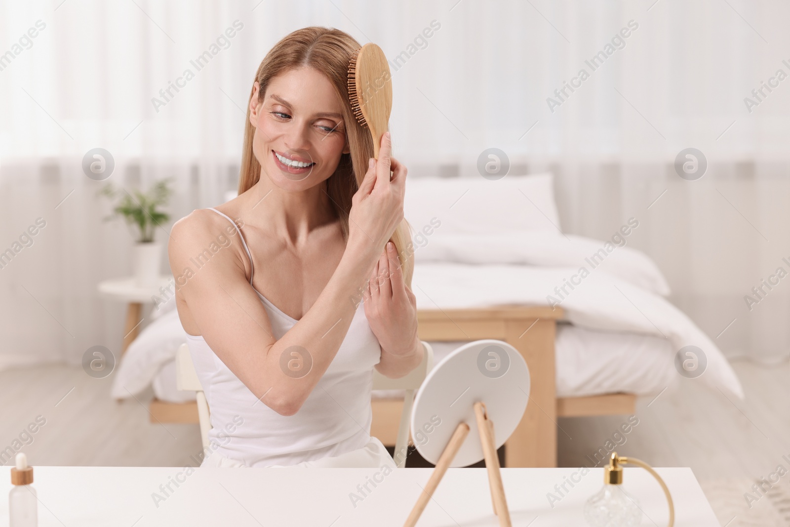 Photo of Beautiful woman brushing her hair at vanity in bedroom