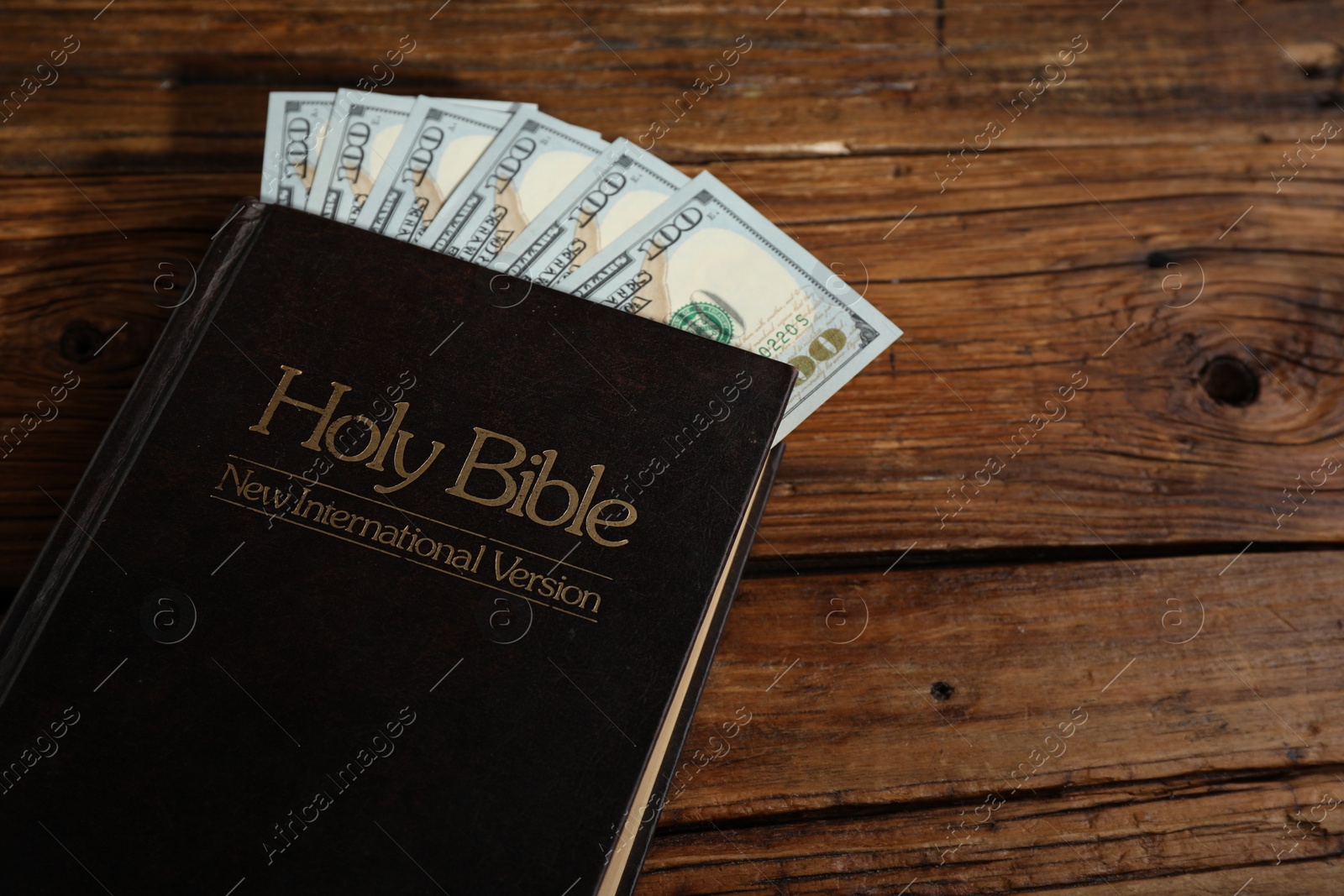 Photo of Holy Bible and money on wooden table, closeup. Space for text