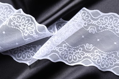 Photo of Beautiful white lace on black fabric, top view