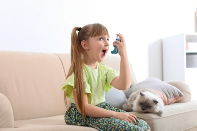 Photo of Little girl using asthma inhaler near cat at home. Health care