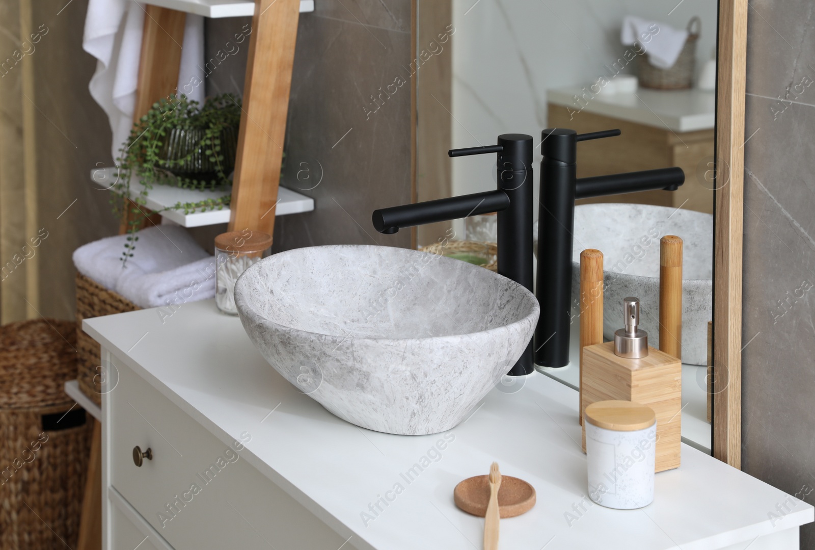 Photo of Stone vessel sink with faucet and toiletries on white countertop in bathroom