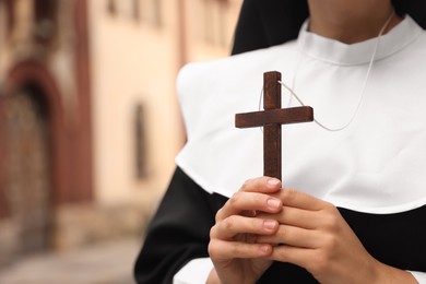 Photo of Young nun holding Christian cross near building outdoors, closeup. Space for text