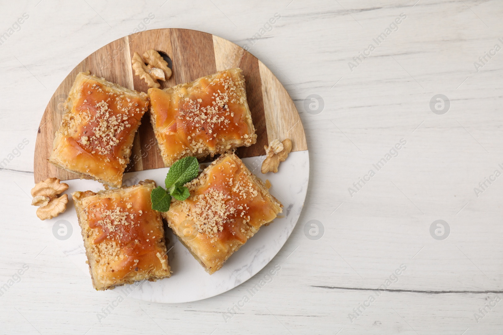 Photo of Eastern sweets. Pieces of tasty baklava on white wooden table, top view. Space for text