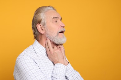Photo of Senior man suffering from sore throat on yellow background, space for text. Cold symptoms