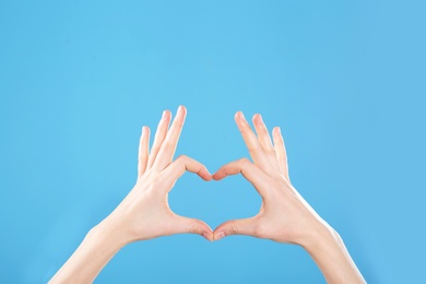 Woman making heart with her hands on color background, closeup