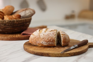 Photo of Wicker bread basket with freshly baked loaves and knife on white marble table in kitchen