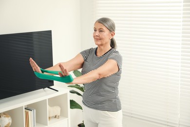 Photo of Senior woman doing exercise with fitness elastic band at home