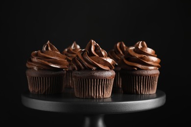 Photo of Delicious chocolate cupcakes with cream on dessert stand against black background