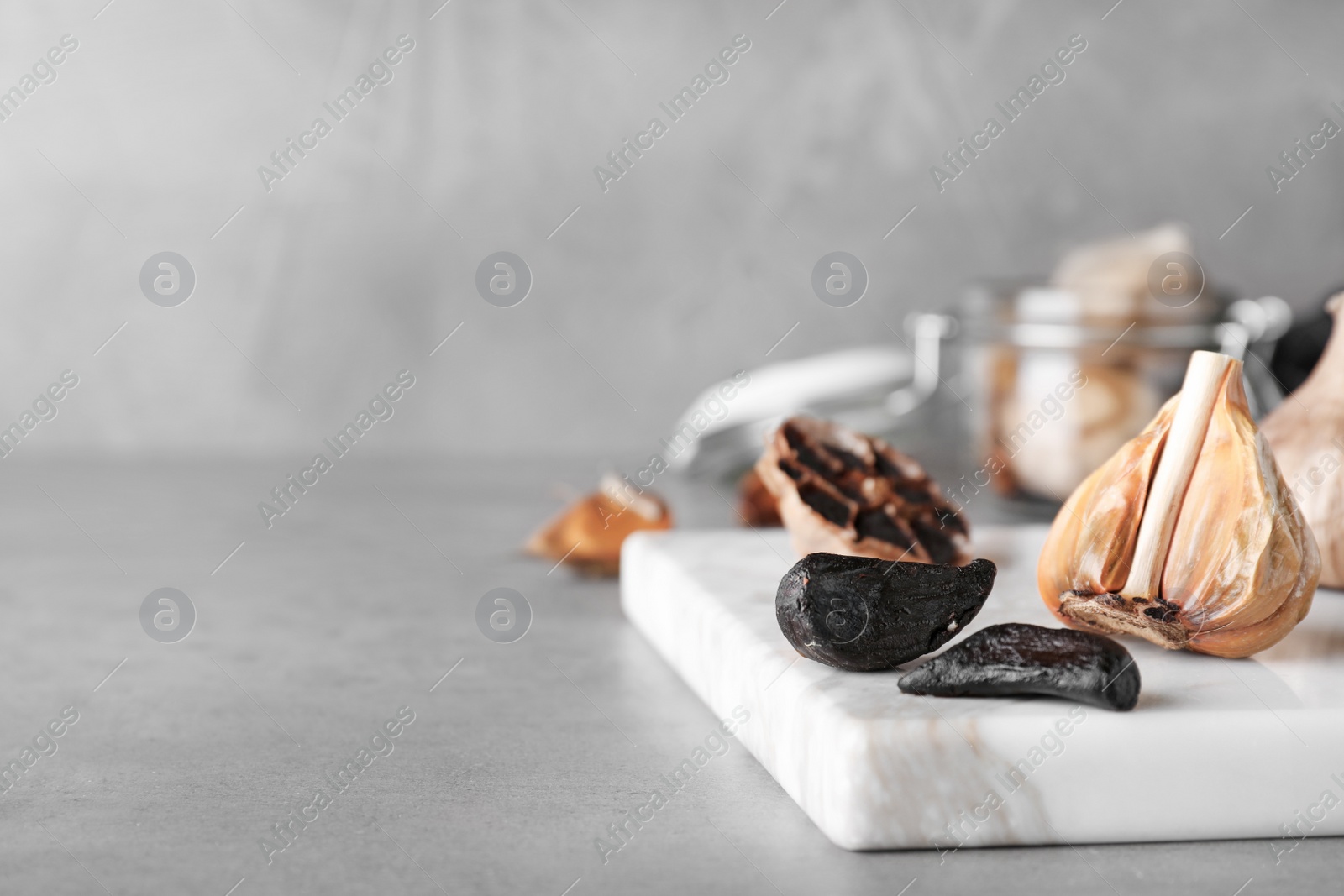 Photo of Marble board with black garlic on grey table. Space for text