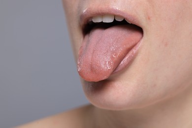 Woman showing her tongue on grey background, closeup. Space for text