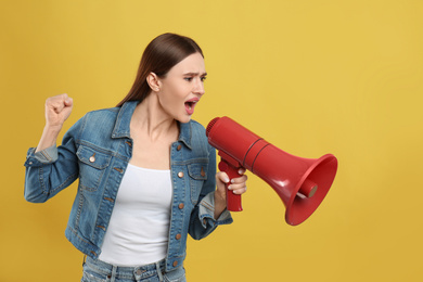 Emotional young woman with megaphone on yellow background