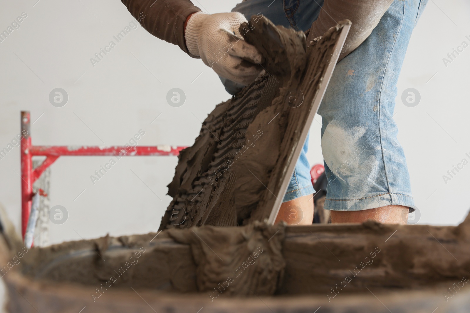 Photo of Worker applying cement on wall tile for installation indoors, closeup