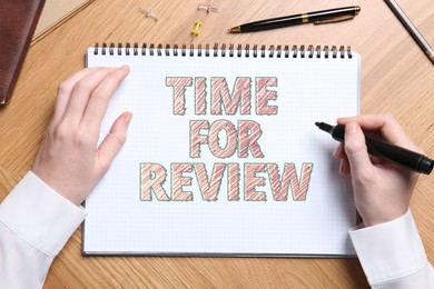 Woman writing text Time For Review at wooden table, closeup. Top view