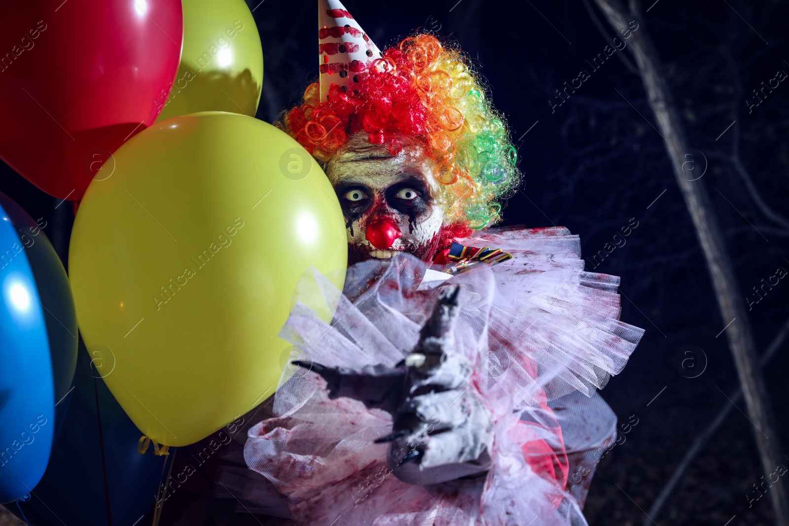 Photo of Terrifying clown with air balloons outdoors at night. Halloween party costume