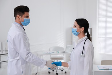 Doctors in medical gloves with protective masks giving handshake at hospital