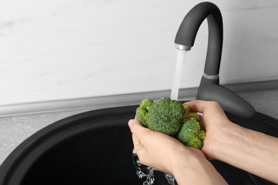 Photo of Woman washing fresh green broccoli in kitchen sink, closeup view. Space for text