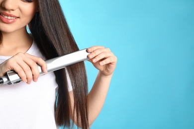 Happy woman using hair iron on color background, closeup. Space for text