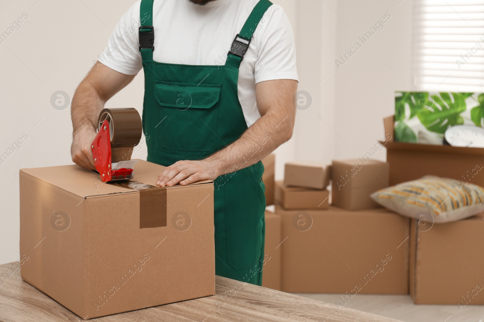 Photo of Man packing box with adhesive tape indoors, closeup. Moving service