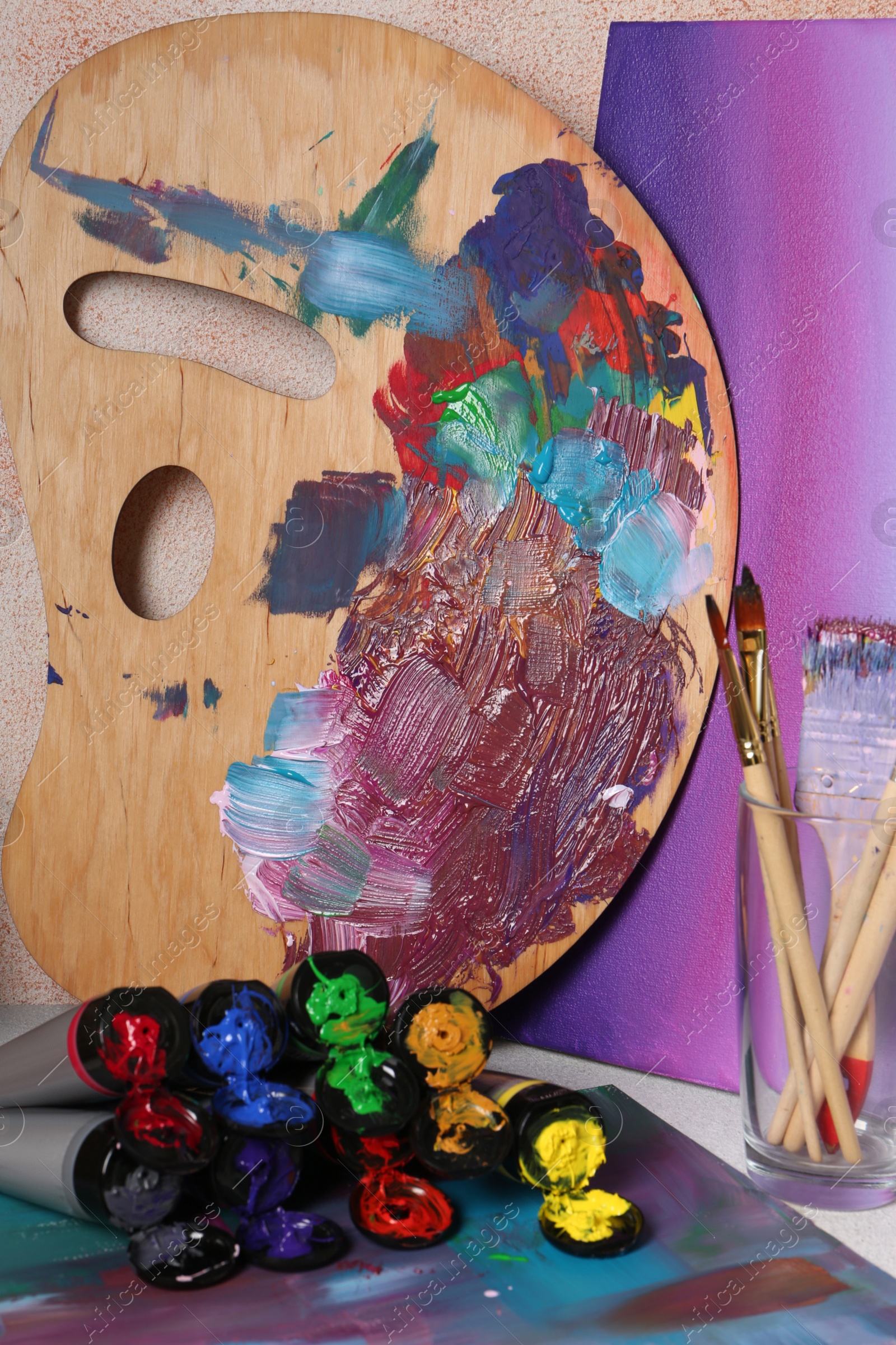 Photo of Wooden artist's palette with colorful paints and brushes on table