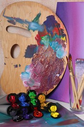 Wooden artist's palette with colorful paints and brushes on table