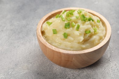 Photo of Bowl of tasty mashed potato with greens on grey marble table, closeup. Space for text