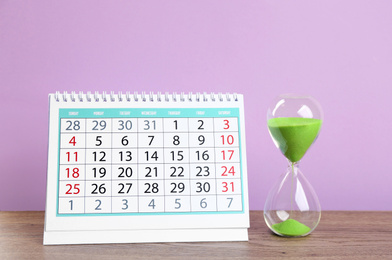 Photo of Calendar and hourglass on wooden table against violet background