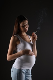 Pregnant woman smoking cigarette on black background