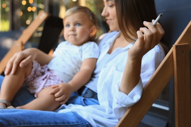 Mother with cigarette and child outdoors, focus on hand. Don't smoke near kids