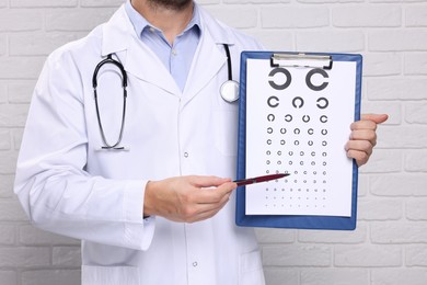 Ophthalmologist pointing at vision test chart near white brick wall, closeup.