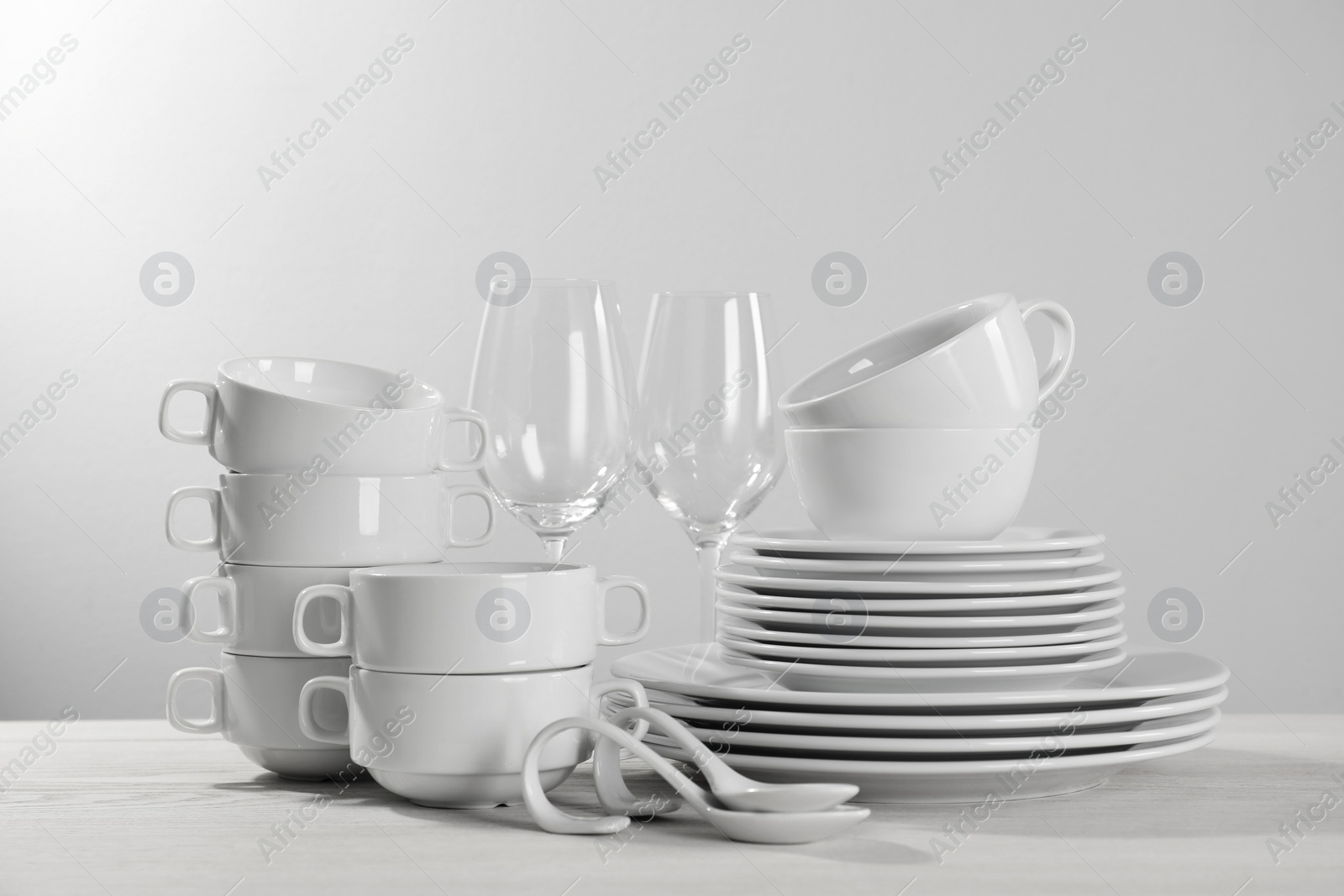 Photo of Set of clean dishware and glasses on white wooden table against light background