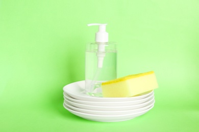 Photo of Detergent, plates and sponge on green background. Clean dishes