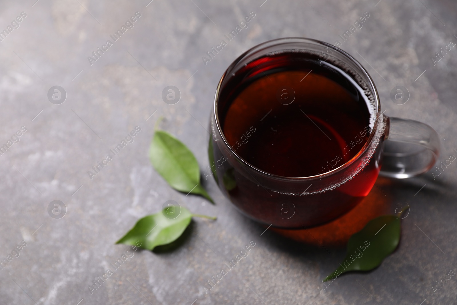 Photo of Tasty hot tea in cup and leaves on grey table, closeup. Space for text