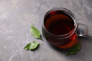 Photo of Tasty hot tea in cup and leaves on grey table, closeup. Space for text