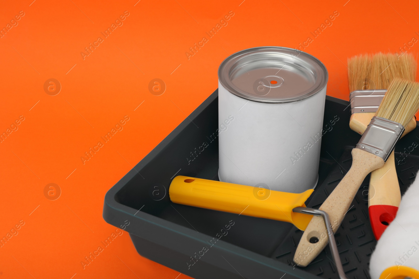 Photo of Can of orange paint, brushes, roller and container on color background. Space for text