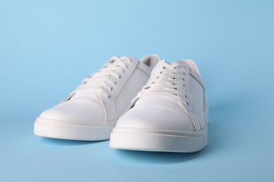 Pair of stylish white sneakers on light blue background