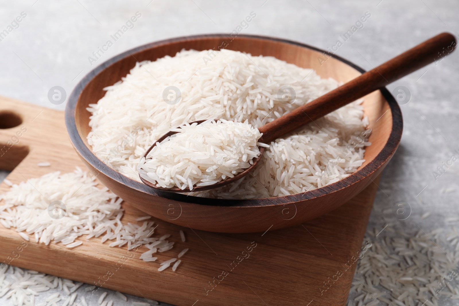 Photo of Raw basmati rice in bowl and spoon on grey table