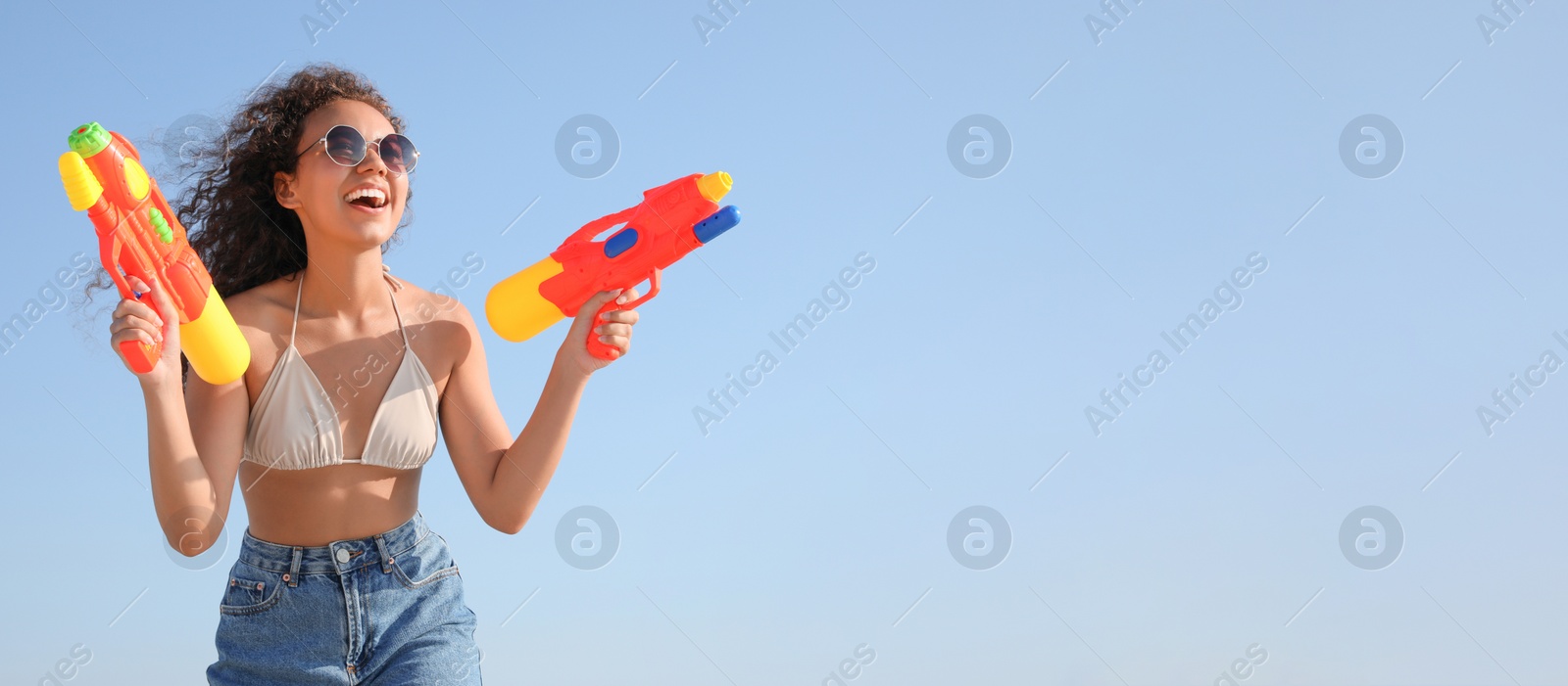Photo of African American woman with water guns having fun against blue sky