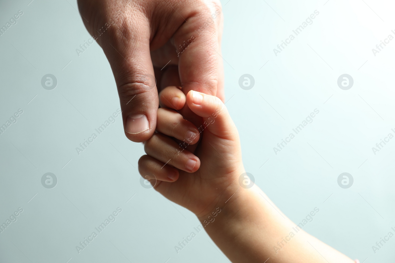 Photo of Father and child holding hands on light blue background, closeup