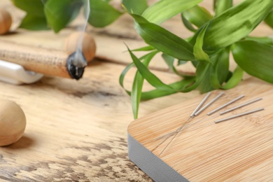 Photo of Wooden board with needles for acupuncture on table, closeup