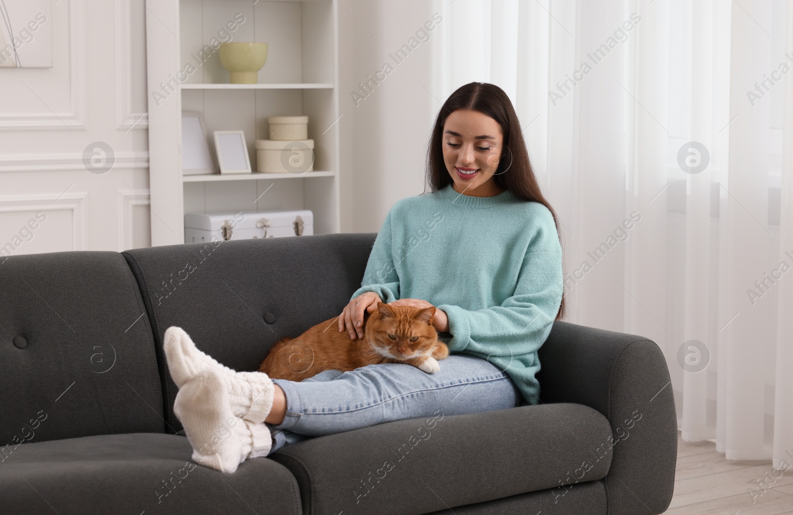 Photo of Beautiful woman petting cute cat on sofa at home