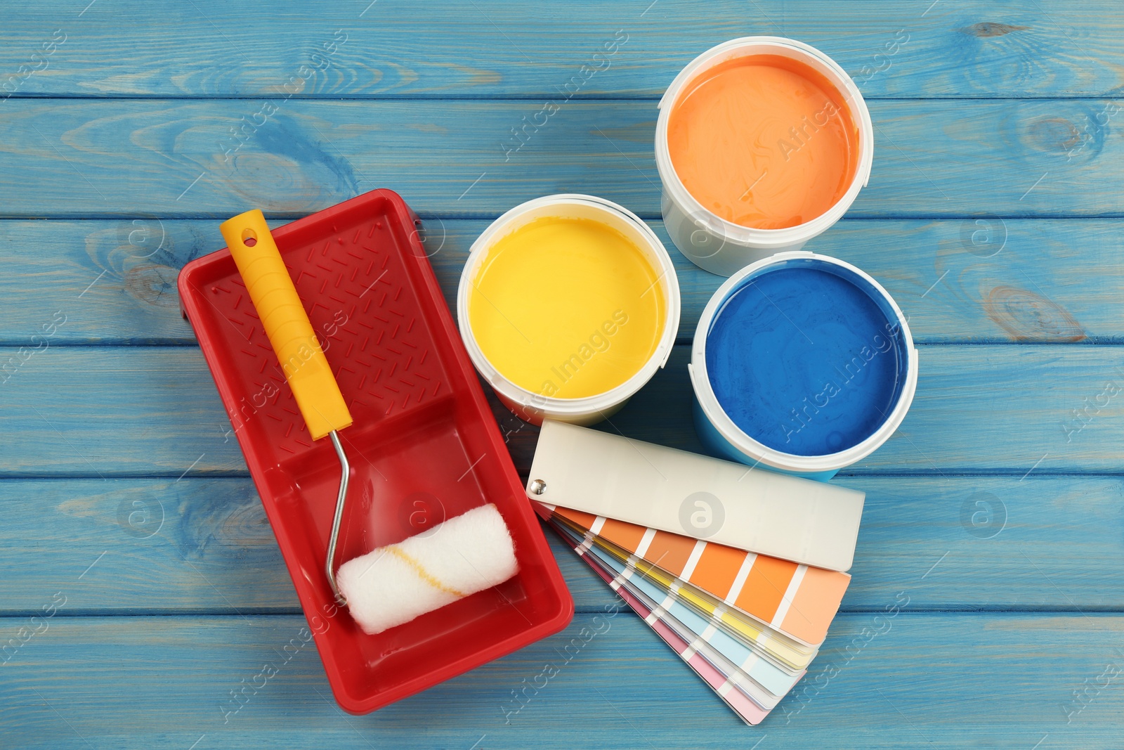 Photo of Buckets of paints, palette and decorator's tools on blue wooden background, flat lay